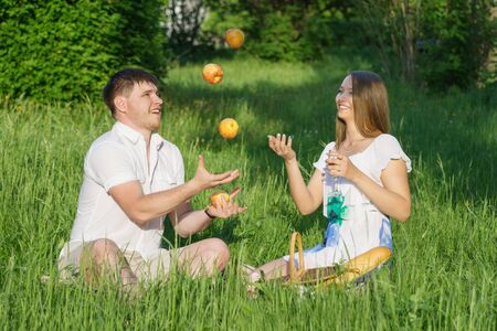 The young man juggling apples with girl during a picnic in a city parkの写真素材