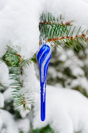 Blue Christmas toy on a fir branch covered with snow outdoorsの写真素材