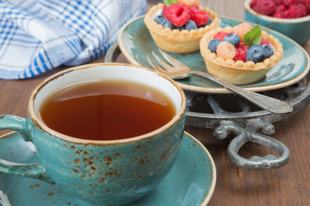 Black tea in a blue vintage cup and fruit tartlets with raspberries and blueberriesの写真素材