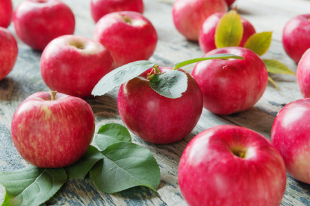 Many red apples with green leaves lie on the old wooden tableの写真素材
