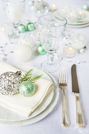 Silver knife and fork, beautiful wine glass, and green christmas balls lie on the white porcelain plate, which is located on a table covered with a white tableclothの写真素材