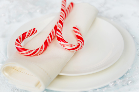 Two red and white striped candy canes lie on linen napkin placed on a white porcelain plateの写真素材
