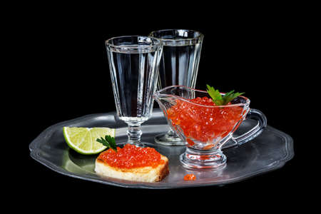 Sandwiches with red caviar and two glasses of vodka on a pewter plate isolated at blackの写真素材