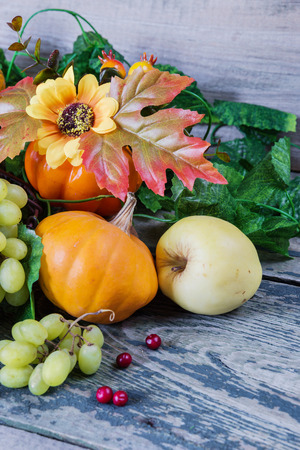 Autumn Still Life: green grapes in a basket and ripe apples, red cranberries, orange decorative pumpkin and squash with leaves on the wooden backgroundの写真素材