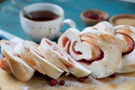 Sweet sliced homemade bun with a cowberry jam and a cup of tea
