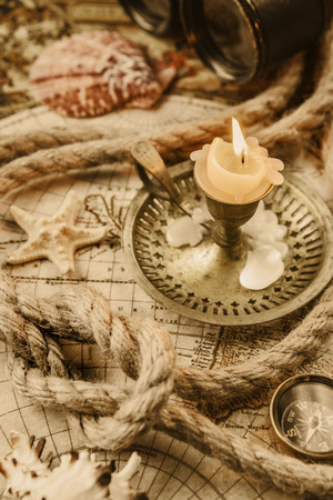 Burning candle, compass, starfish, binoculars and the ship's rope located on the background of old mapの写真素材