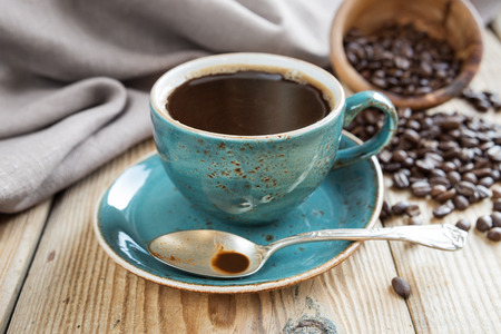 Blue cup of black coffee and scattered coffee beans on a background of a linen clothの写真素材