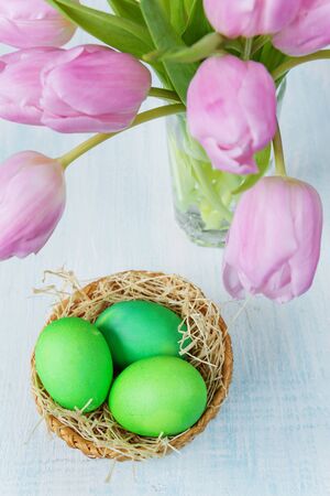 Three green Easter eggs in a basket and a bouquet of pink tulips flowersの写真素材