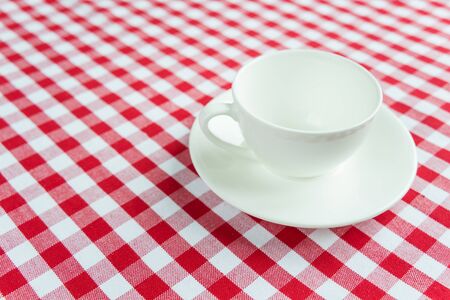 Empty white porcelain cup on a background of red and white checkered clothの写真素材