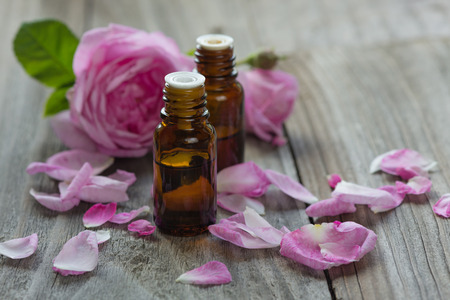 Two vials with essential oil and petals of pink roses on a wooden backgroundの写真素材