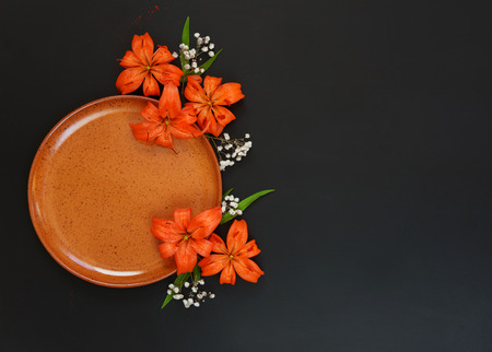 Beautiful orange flowers lilies and clay plate, isolated on a black backgroundの写真素材