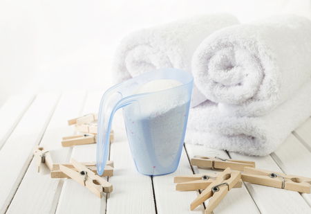 Rolls of white fluffy bath towels, washing powder in measuring cup and wooden clothespins on the...