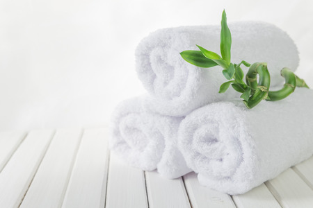 SPA concept: stack of three rolls of white fluffy bath towels with green Lucky bamboo plant on the background of white boardsの写真素材