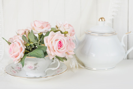 Beautiful still life: a graceful porcelain cup, white china teapot and pink rose flowersの写真素材