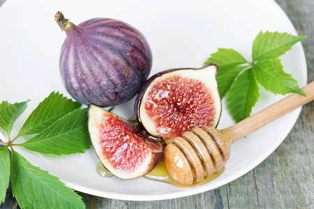 Ripe figs, fresh honey and beautiful green leaves are on a white porcelain plateの写真素材