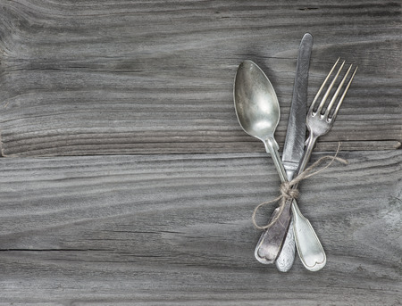 Crossed vintage fork, table knife and spoon on old wooden boardsの写真素材