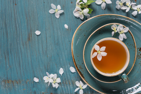 Blue ceramic cup of green tea and apple-tree flowers on an old blue wooden shabby background with copy-spaceの写真素材