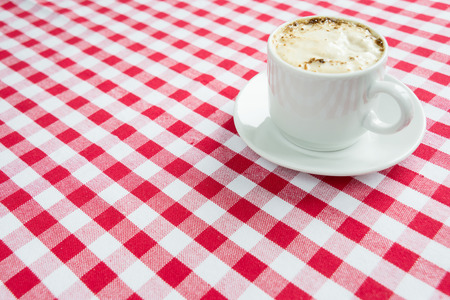 Black coffee with rich crema in a white porcelain cup on a background of red and white checkered cloth, with space for textの写真素材