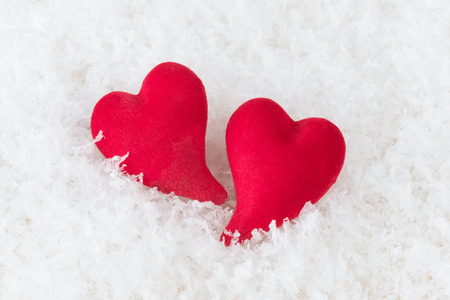 Two red hearts lie on white puffy cold snow. Metaphor of love. Greeting card for Valentine's Dayの写真素材