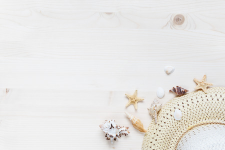 Concept of a beach holiday: straw hat and seashells are on a light wooden surface. Top view, flat...
