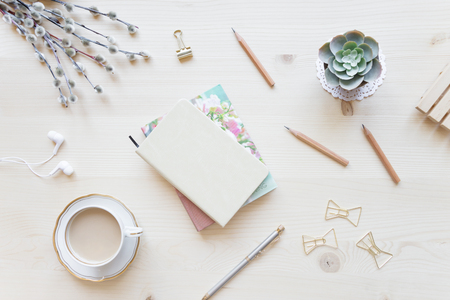Female home office desk table in pastel tones. Workspace with notebooks, cup of coffe and decorations on light wooden background with copy-space. Flat lay, top viewの写真素材