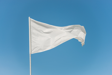 White flag against the blue sky fluttering in the windの写真素材