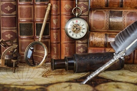 Vintage pocket watch, navigation instruments  and silver pen are on the background of antique books