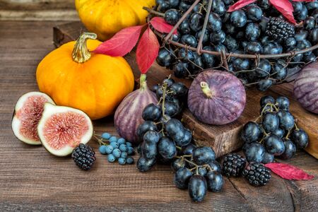 Black grapes in a basket and ripe figs, red raspberries, orange pumpkin and blackberries with autumn leaves on the wooden backgroundの写真素材