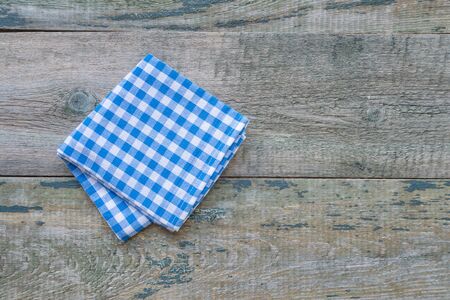 Checkered blue-and-white napkin is on a rough background of wooden table, with space for textの写真素材