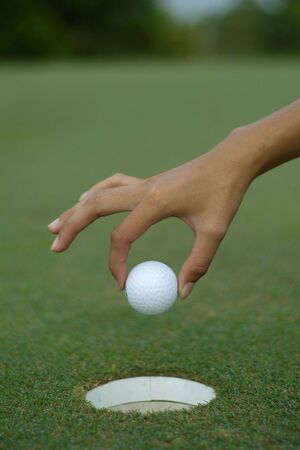 Hand dropping a golf ball into the holeの写真素材