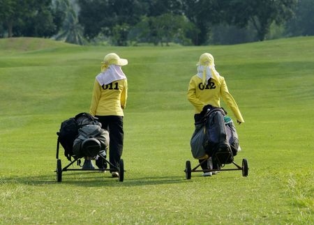 Two caddies walking down the fairway of a golf course in Thailandの写真素材