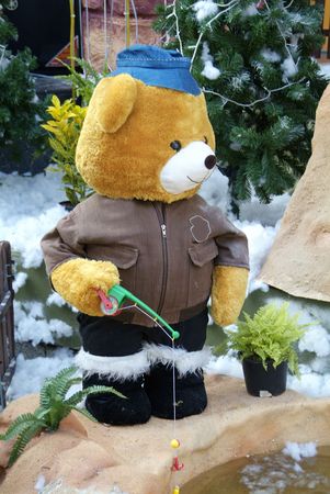 Teddy-bear in winter clothing fishing at a small pondの写真素材
