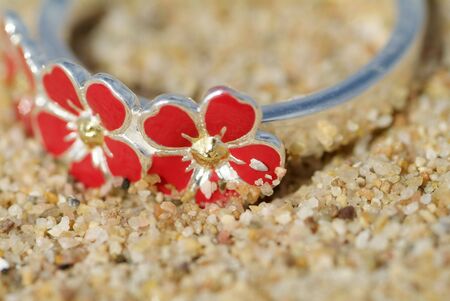 Detail of silver ring with red enamel flowers in the sand. Very shallow depth of field.の写真素材