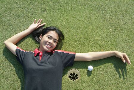 Young, female golf player smiling and embracing the hole at a colf course.の写真素材