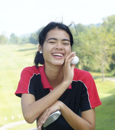 Yeoung, female golf player smiling, holding golf club and ball, with fairway in the background.の写真素材