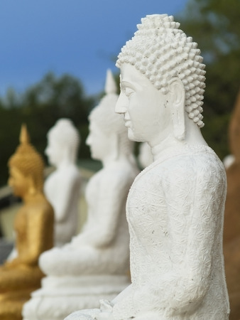 White Buddha image at a Buddhist temple in Thailand. Two white and a golden, out of focus Buddha images in the background.の写真素材