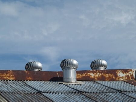Three wind-driven, rotating ventilators on a corrugated steel roofの写真素材