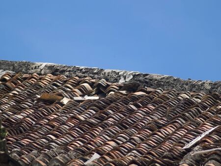 Roof tiles of an old, damaged villa with a blue sky background.の写真素材