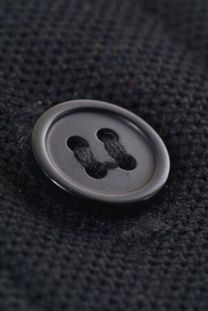 Small, black button on black fabric. Macro photography with extreme detail and shallow depth of field.の写真素材