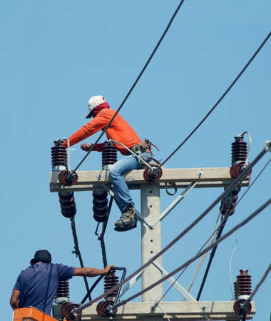 Silhouette men performing maintenance work on a pole for electric wiring. の写真素材