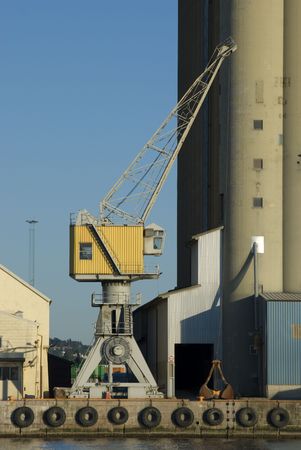 Crane at a harbour, between a warehouse and a silo.
