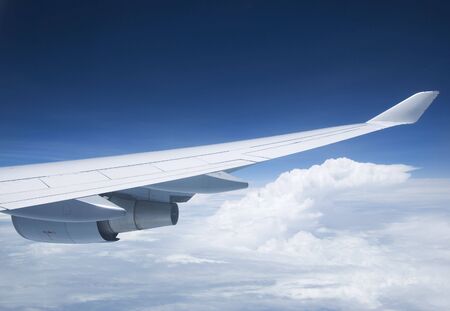 Wing and jet engine of passenger airplane flying, with a white clouds and dark blue sky background.