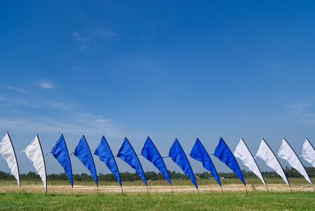 Blue and white flags on a field of grass, with a blue sky background.の写真素材