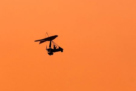 Silhouette of microlight aircraft on an orange backgroundの写真素材