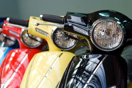 Headlights of three scooters, black, yellow and red. Shallow depth of field with the first scooter in focus.の写真素材