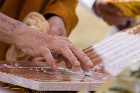 Hand of Buddhist monk painting religious symbols with his finger. Shallow depth of field.の写真素材