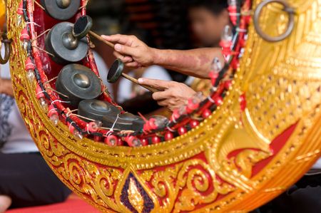 Gong Mon, a traditional Thai instrument particularly used in funerals, with the hands of a man playing. Shallow depth of field with focus on the nearest hand.の写真素材