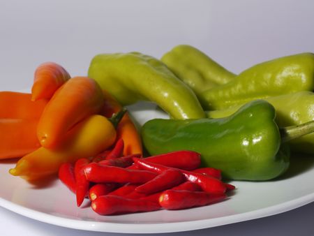 Red, orange and green chili peppers from Thailand on a white plate. Shallow depth of field with the nearest peppers in focus.の写真素材