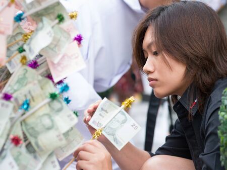 BANGKOK - DECEMBER 23: Woman giving alms in form of a 20 baht note during a mass alms giving in the morning at Soi Thonglor in celebration of the 2,600th anniversary of Lord Buddha's enlightenment on December 23, 2012 in Bangkok, Thailand.のeditorial素材