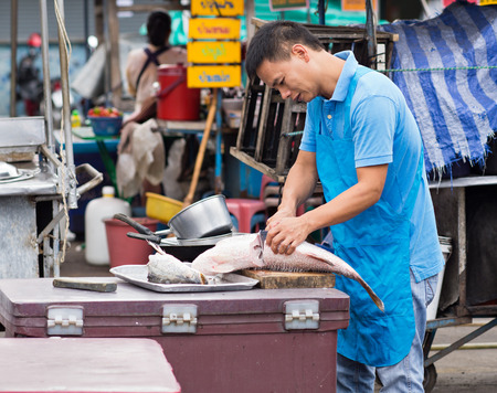 PATTAYA, THAILAND - NOVEMBER 27, 2014: Market vendor slicing a fish before opening his restaurant at an outdoor market in Pattaya City.のeditorial素材